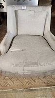 Front view of grey upholstered armchair showing extensive fabric tears and wear on the seat cushion