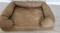 Front view of large brown rectangular dog bed with padded side bolsters on carpeted floor.