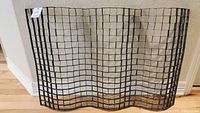 Rectangular metal wall art sculpture with grid pattern, leaning against a wall on wood floor