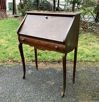 Antique wooden secretary-style desk with closed slant front and drawer.