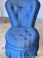Front view of blue upholstered slipper chair showing button tufting on backrest and seat, fabric texture, and skirted base.