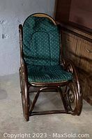 Wooden cane back rocking chair with green removable cushioned seat and back, showing curved armrests and scroll details on rockers.