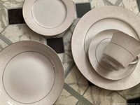 Photo showing set of plates and cup with saucer exhibiting the white china with the embossed Lovelace floral scroll pattern and silver trim.