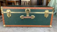 Front view of Concourse travel trunk showing green body, leather trim, brass locking mechanisms, and 'Concourse' label.