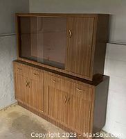 Two-piece Mid-Century Modern wood-toned china cabinet with glass sliding doors on the upper section and side liquor cabinet, lower storage cabinets, original gold-tone hardware handles.