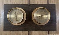 Wall-mounted nautical thermometer and humidity meter on wood plaque.