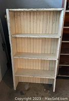 Front-facing photo of a painted wooden shelf unit showing four shelves with beadboard back panel. Paint is chipped and worn with visible signs of age and disuse.