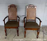 Photo showing two wooden dining chairs with cane backs and green velvet upholstered seats, positioned side by side on a concrete floor.