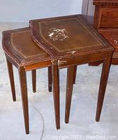 Photo showing two wooden nesting tables stacked, both with worn surfaces and visible damage on the larger one.