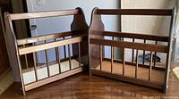 Two identical vintage wooden magazine racks side by side on a wooden surface. Both racks have vertical slats on the front and back, with curved side panels serving as handles. The wood has a medium brown finish with some visible wear.
