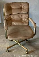 Brown upholstered office chair with a tufted cushioned backrest, padded armrests, and a five-star gold metal wheeled base.