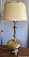 Full view of vintage table lamp showing amber glass globe base, metal footed base, and original beige fabric shade