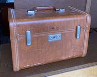 Closed brown vintage ladies travel case showing handle, metal clasps, and locking mechanism. Exterior shows signs of wear near bottom edges.