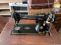 Side view of black Singer sewing machine with gold detailing mounted in cabinet surface.