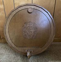 Front view of closed wooden barrel-shaped mini bar with carved emblem and wooden tap.