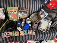 Entire lot laid out on striped couch showing all items including cards, plates, mugs, caps, encyclopedia and framed memorabilia