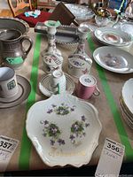 View of multiple vintage china items including demitasse cup and saucer, lidded containers, candle holders, plates including one decorated with 'February' and violets.