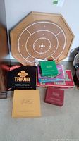 Wooden Crokinole board leaning against wall with multiple game boxes in front including Trivial Pursuit, Canada Trivia, and other boxed games.