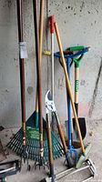 View of the set showing the rake, shovel, pruners, aerator, edger and sprinkler grouped together on concrete floor against wall.