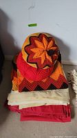 Photo of stacked crocheted pillow, red blanket, and crocheted afghan with warm colored chevron pattern