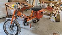 Front-left angle view of orange moped showing frame, seat, front fender and handlebars