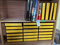 Wooden shelf with 26 National Geographic magazines in protective sleeves showing yellow spines with title and dates, along with additional National Geographic books on top shelf.