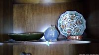 Photo showing three pottery items on a shelf: an owl figurine, a decorative plate with floral pattern, and a shallow dish