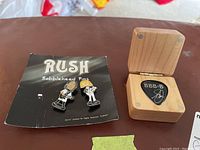Wooden box open with two enamel bobblehead pins on card to left and pick slot visible