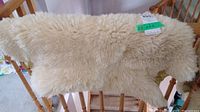 Sheep skin rug draped over wooden railing showing overall shape and cream color.