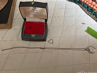 Silver heart necklace laid out with heart locket, metal heart charm, and open presentation case.