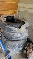 Stack of four tires wrapped in plastic, two stacked on two