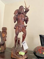 Full view of carved wooden statue depicting a man holding an animal on his shoulders with a deer behind and a dog at his feet.