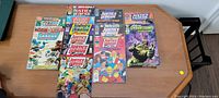 14 comic books laid out on table, showing covers with various superheroes from Marvel and DC Comics series like Justice League and Swamp Thing.