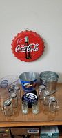 Full lot showing Coca-Cola wall decor, two metal buckets, glass jars, salt shakers, glass pitcher and clamato container.