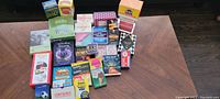 Image showing 28 packages of adult card games arranged on a wooden table including various colorful boxes mainly of card games.