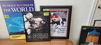 Four mounted sports posters displayed on furniture; includes the Rothmans Racing F1, Georges St-Pierre MMA, Sports Illustrated NFL cover, and cycling art posters.
