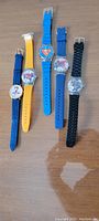 All five watches laid out together on a brown surface showing colors and character faces.