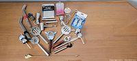 Full view of assorted metal bar tools including strainers, jiggers, corkscrew, openers and spoons on a wooden surface.