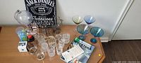 Wide shot of all bar paraphernalia items arranged on a wooden table, showing various glassware, Jack Daniel's sign, globe-shaped dispenser, and books.