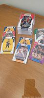Photo shows several colorful NBA Hoops basketball trading cards featuring different NBA players laid out on a wooden surface with some cards stacked in a plastic holder.