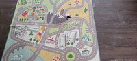 Top view of children's play rug showing colorful road map design including roads, buildings, mountains, tents, and vehicles.