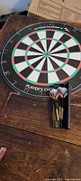 Front view of the Player's Choice dartboard on a wooden surface with darts in a container.