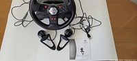 Photo showing Logitech Nascar steering wheel, two foot pedals, associated cables, and a printed manual for QuickCam Communicate STX.