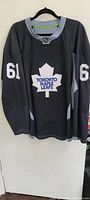 Black and gray training camp hockey jersey with Toronto Maple Leafs white maple leaf logo and number 61 on sleeves hung on hanger.