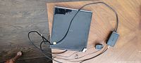 Top view of black square flat panel RCA HD antenna with cables on wooden floor.