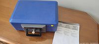 Blue Sentry safe on wooden surface with two keys in lock and instruction manual beside it