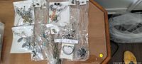 Overview of the unopened costume jewelry lot showing multiple sets of earrings, necklaces, and bracelets packaged in plastic bags on a wooden table.
