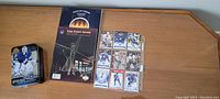 Two souvenir books and an Upper Deck tin box on a wooden table.