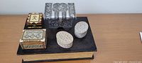 Photo of six trinket boxes on top of a vintage embossed black book, showing various sizes and materials.