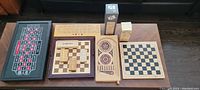 Top view of all wooden board games displayed on floor with clear view of cribbage board, domino set, checkers/chess board, wooden dice, and chess clock.